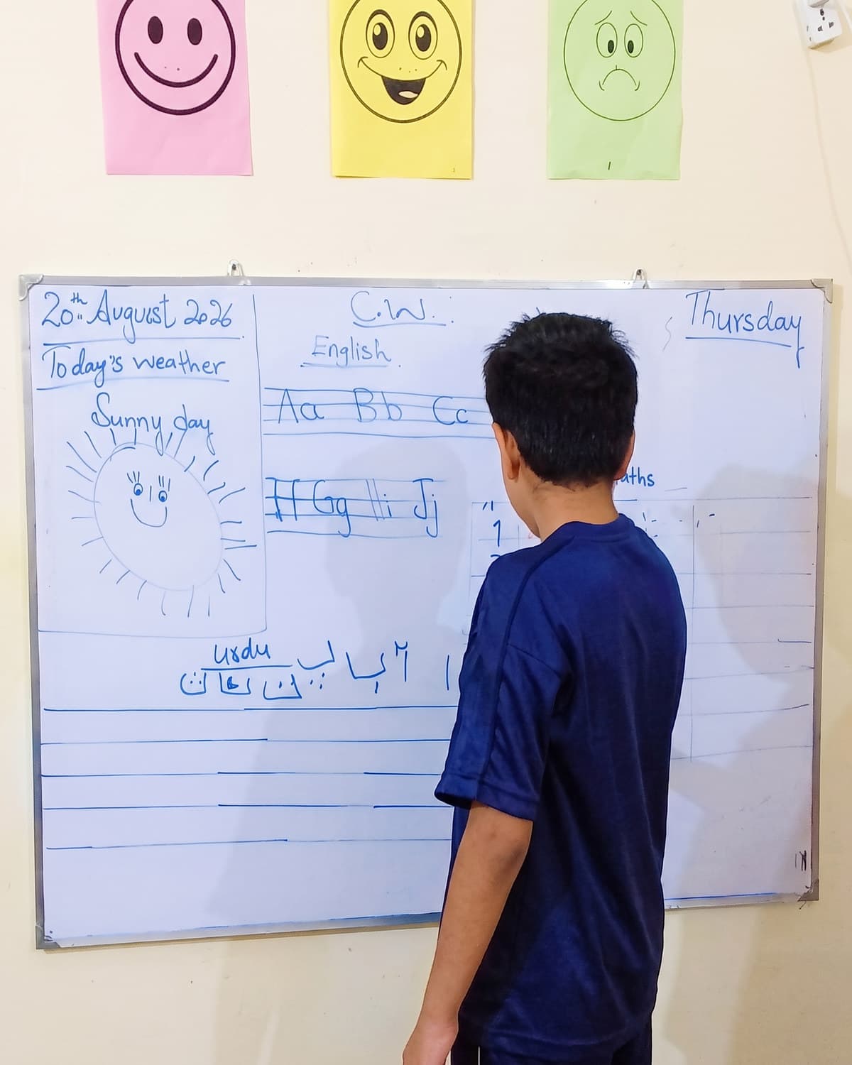 A boy writing on the whiteboard beside the daily schedule