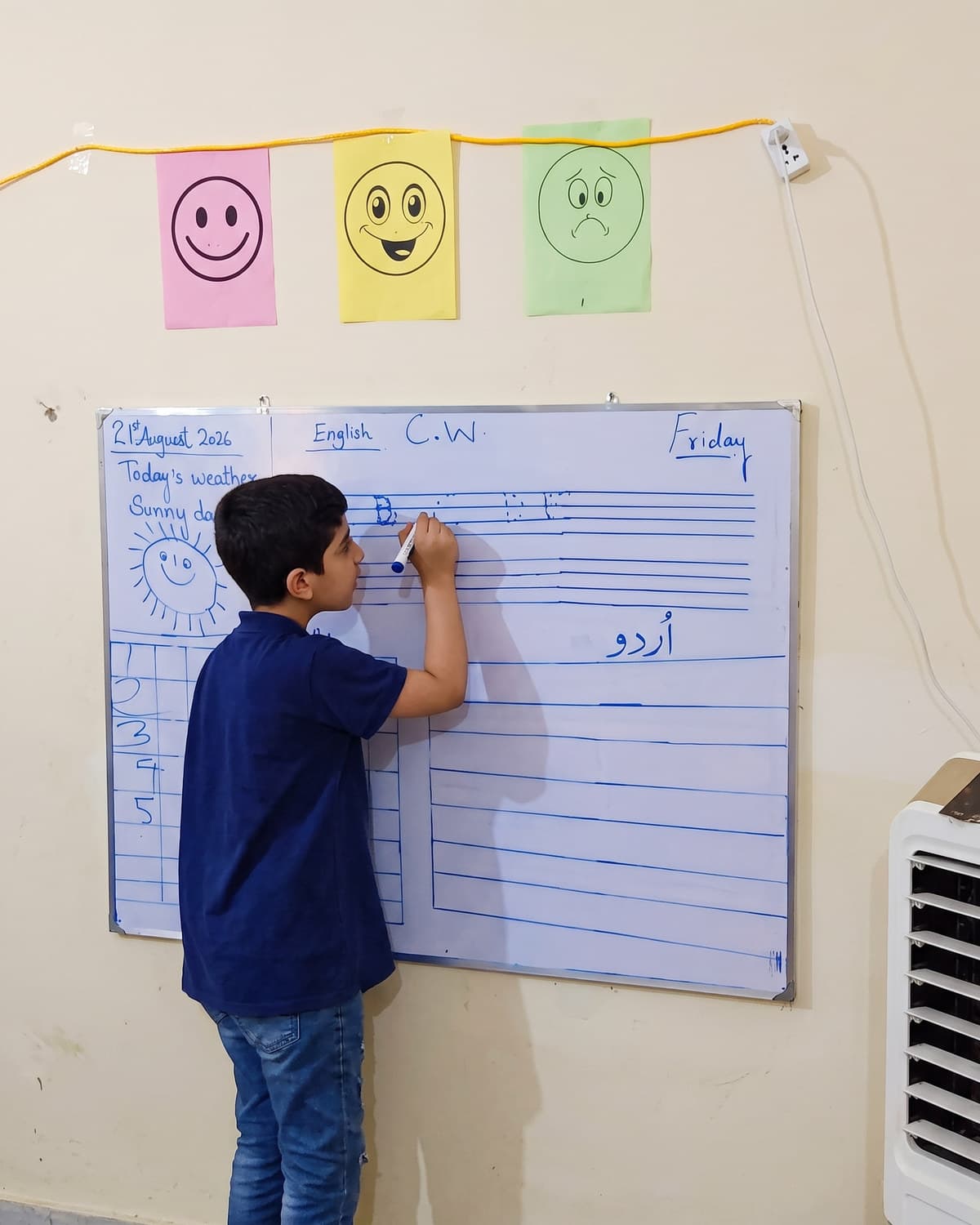 A boy writing on the whiteboard next to the feelings chart
