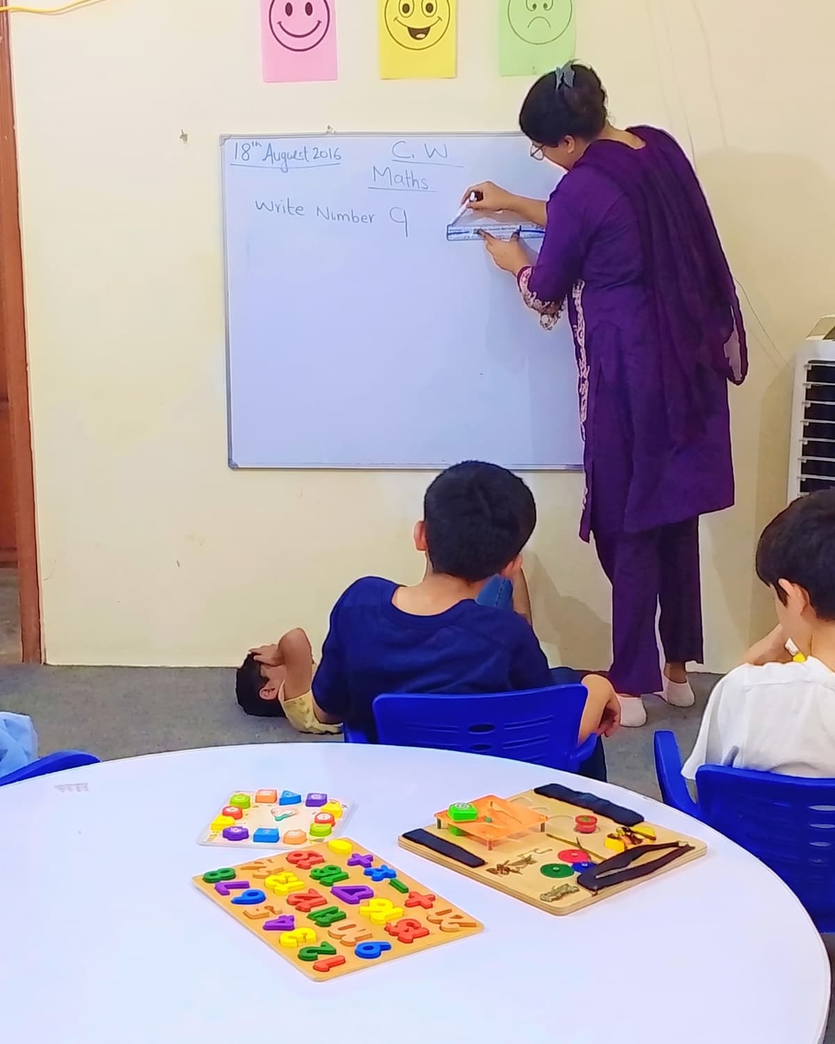A teacher writing on the whiteboard while children work